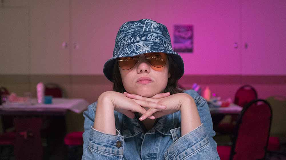 A teenage girls wearing a bucket hat and sunglasses leans on her hands in Sweetheart, a BFI Flare 2021 film.