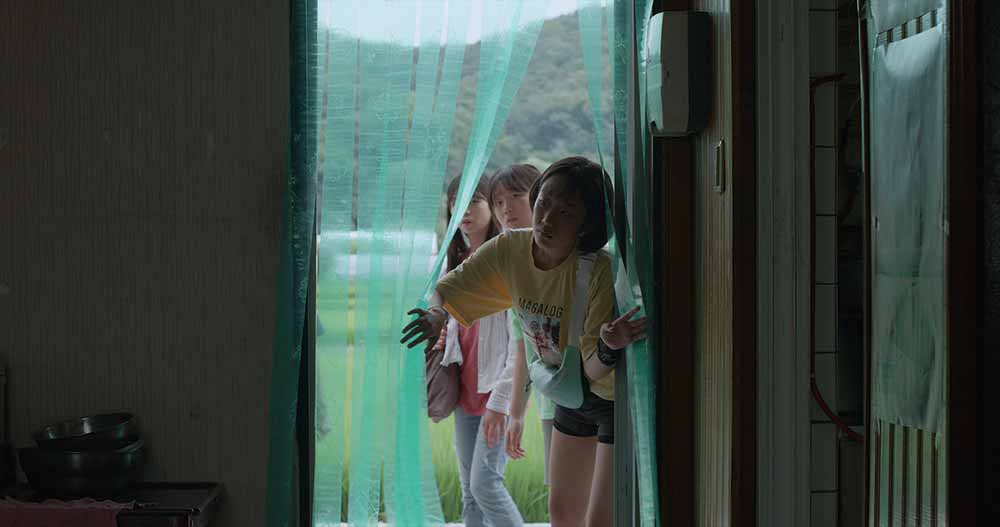 Three young girls peek into a darkened, abandoned house in Short Vacation.