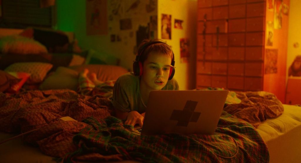 Masha (Maria Fedorchenko) lies on her bed with headphones on, looking at her computer, in Stop-Zemlia, directed by Kateryna Gornostai, which premiered at Berlinale 2021.