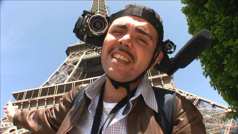 A man stands under the Eiffel Tower, with a camera strapped to his head, in Descent Into Darkness, which screened at the Unnamed Footage Film Festival.
