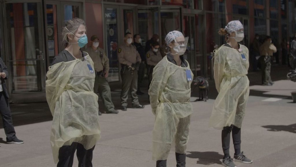 Still from In the Same Breath screening at the 2021 San Francisco International Film Festival. Three women in full PPE stand on the sidewalk in protest.