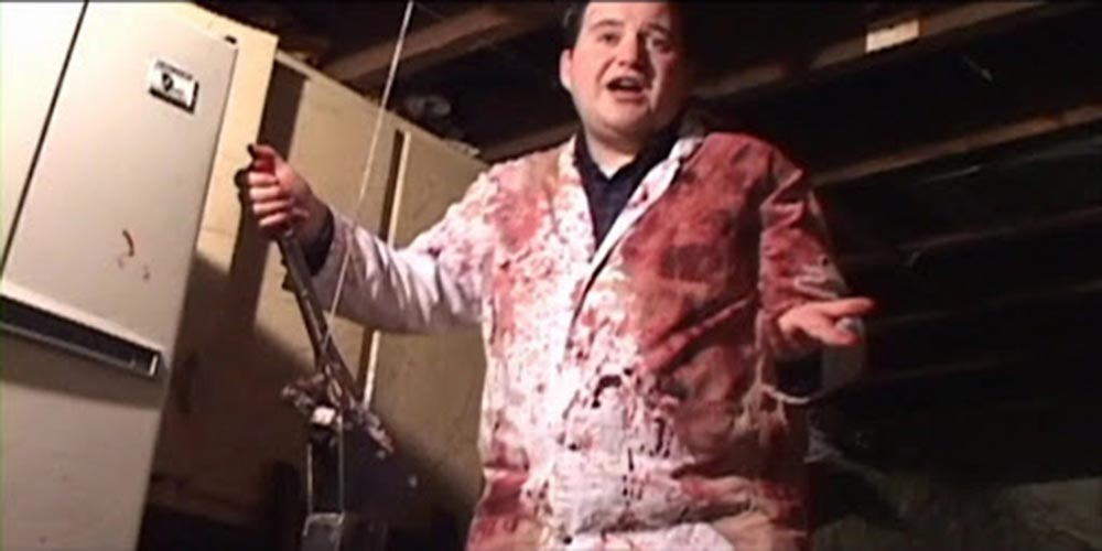 A man wearing blood splattered protective clothing smiles at the camera in Long Pigs, which screened at the Unnamed Footage Film Festival.