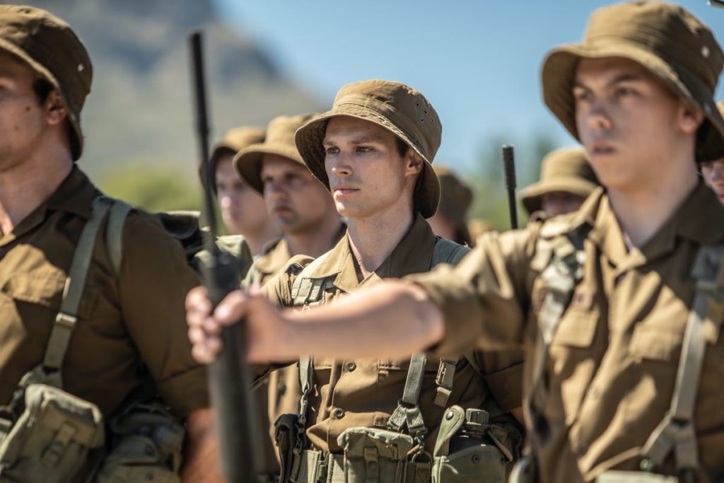 Kai Luke Brummer as “Nicholas” in Oliver Hermanus’ MOFFIE. Courtesy of IFC Films. An IFC Films release. Nicholas is seen holding a gun in formation amidst other conscripts.
