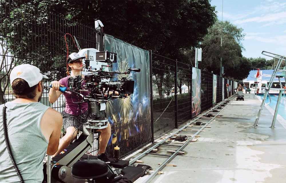 An image of Stéphanie Anne Weber Biron sitting behind a camera on a dolly by an outdoor pool.