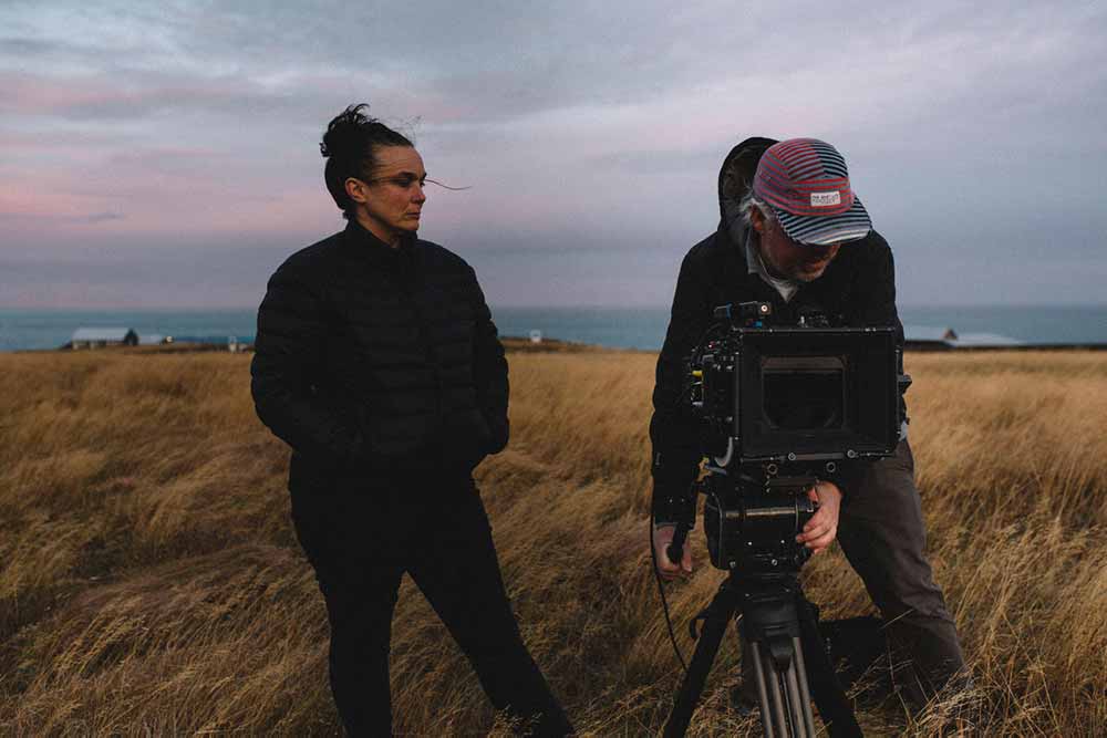 Mylissa Fitzsimmons stands against an Icelandic landscape, next to her DP Todd Hickey, who is looking into a camera.