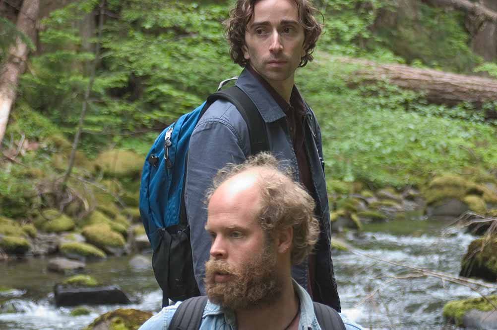 A still of two men wearing backpacks in the woods in Old Joy.