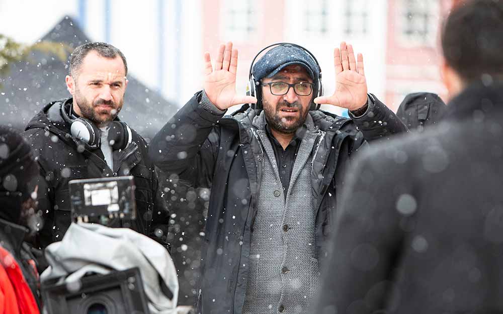Filmmaker Ferit Karahan stands with his camera crew in the snow, motioning with his hands.