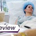 A still from the film Explant, which shows Michelle Visage lying in a hospital bed, recovering from surgery. The text in front of the image reads, "Review".