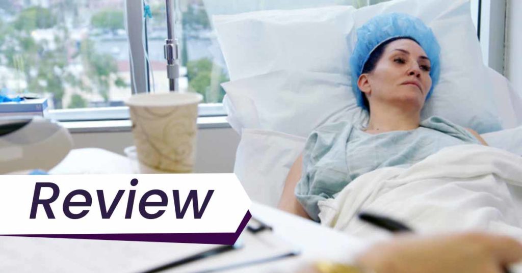 A still from the film Explant, which shows Michelle Visage lying in a hospital bed, recovering from surgery. The text in front of the image reads, "Review".