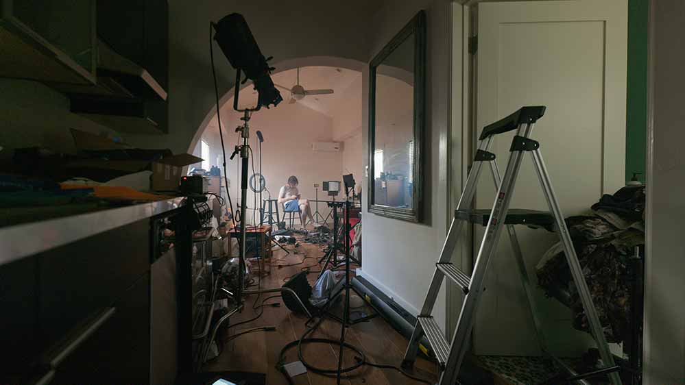 A still of a room full of camera, lighting, and sound equipment, messily strewn around.