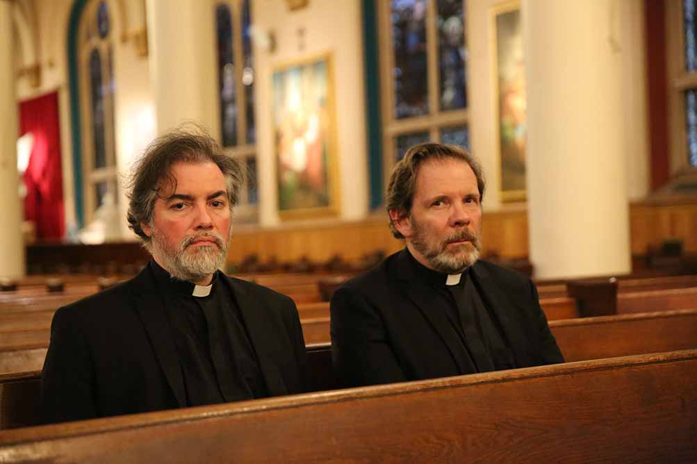 A still from Scenes from an Empty Church, in which two priest site side by side in the pews, in uniform, looking forlornly ahead.