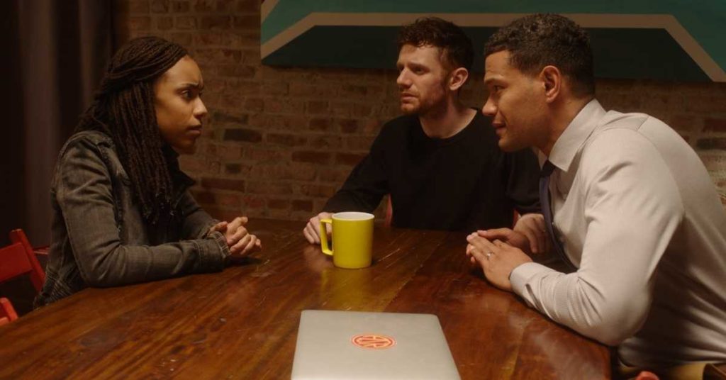 A still in which Jess sits at Josh and Aaron's dining table, and the three somberly speak.