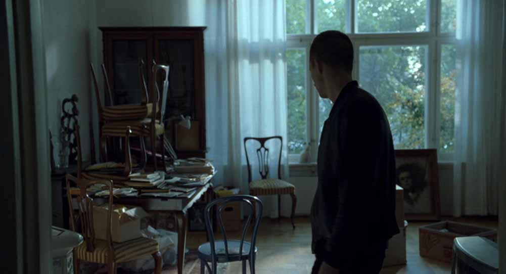 A still from Oslo, August 31st showcasing Jørgen Stangebye Larsen's work on Anders's parents apartment, which is spacious, a bit dark, with chairs scattered everywhere as they're halfway through packing.