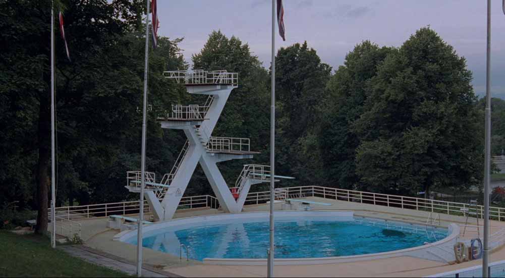 A still featuring a large, circular outdoor pool next to a tall diving board.