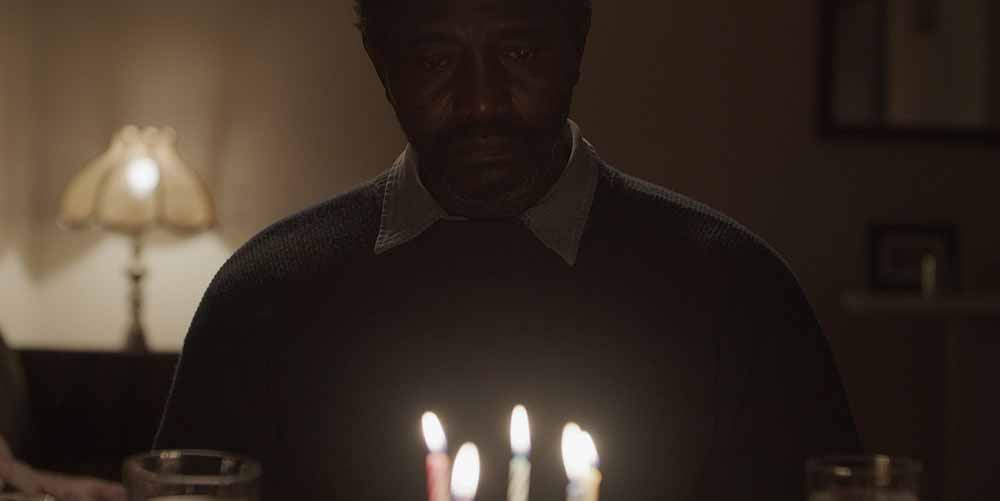 A middle-aged Black man sits in a dark room, in front of a cluster of birthday candles, in Ousmane, one of the best shorts of TIFF 2021.