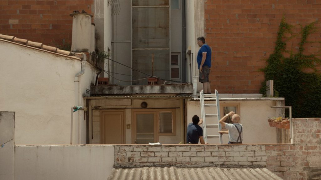 Valero stands on the roof as Moha and Pep hold the ladder in The Odd-Job Men, directed by Neus Ballús.