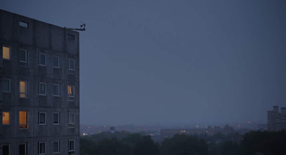 A still from Weekend, shot by Ula Pontikos, in which we see a large tower block against a dusky, blue skyline.
