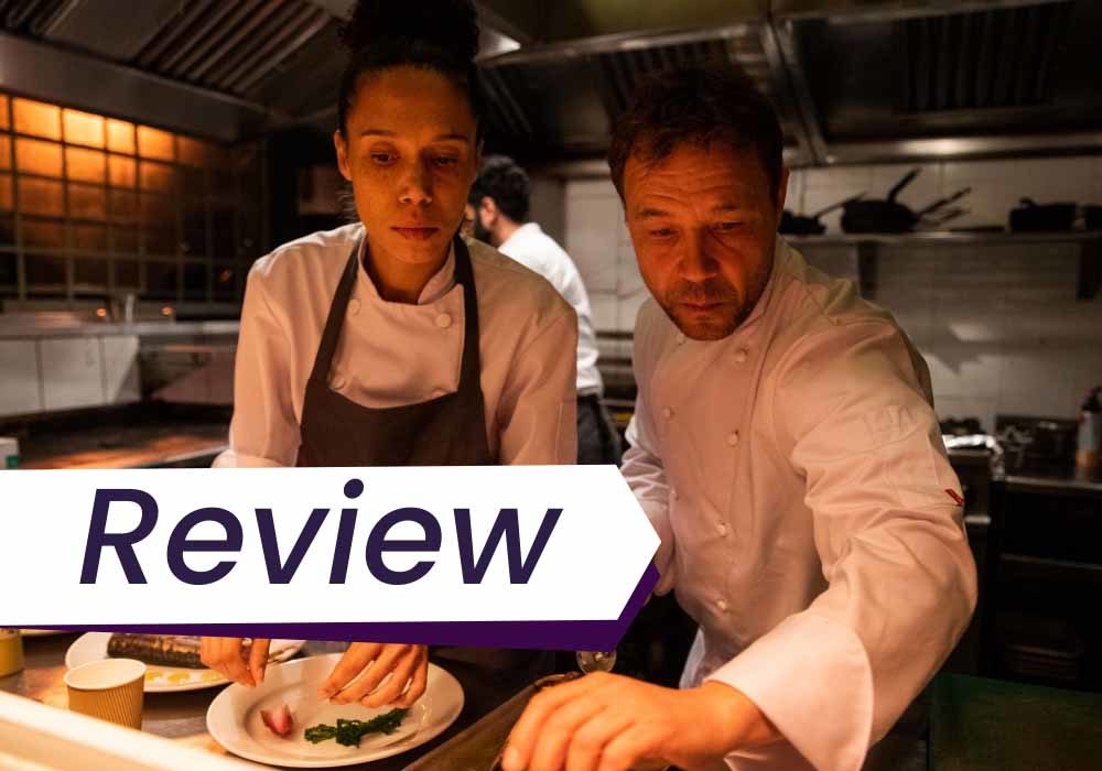 A still from Boiling Point, in which a man, the head chef, and a woman, his sous chef, lean urgently over the kitchen counter, where they are garnishing a dish.