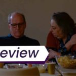 A still from The Humans, in which an aging heterosexual couple sits at a dinner table, the woman looking pointedly at her husband while her looks down at the food in front of him. The text on the image reads, 'Review'.
