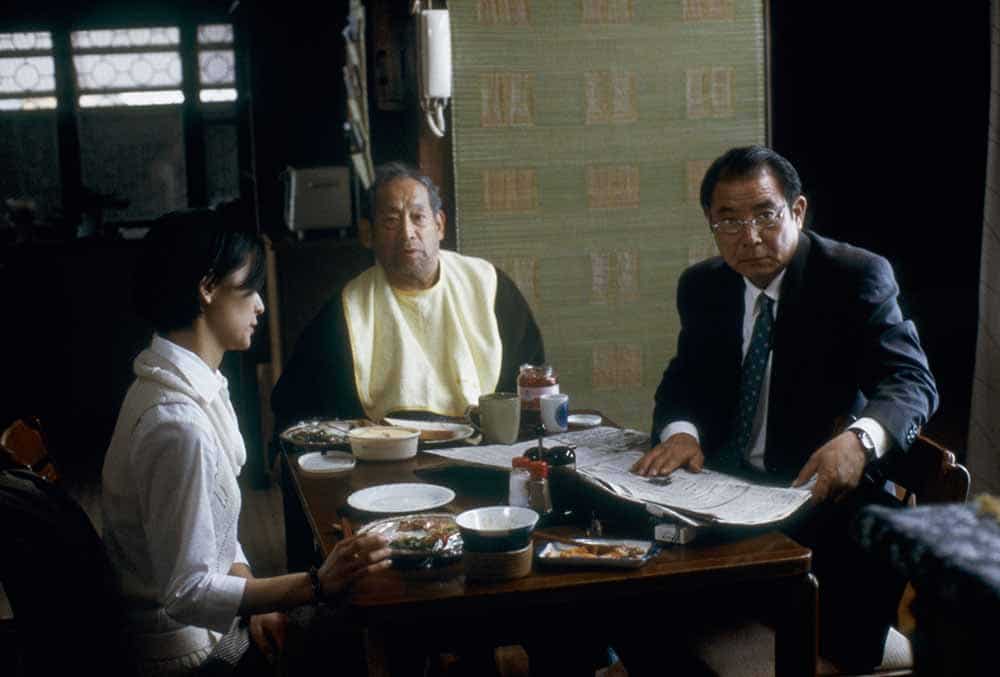 A still from Wild Berries, in which a young woman, her grandfather, and her father, all sit together at the breakfast table.