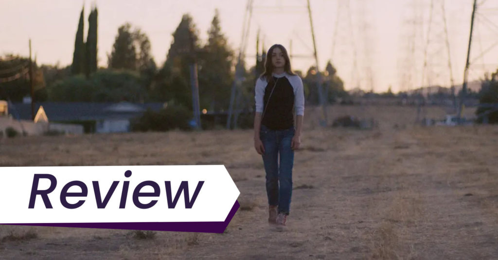 Lily McInerney stars as Lea in Jamie Dack's feature debut Palm Trees and Power Lines, which premiered at Sundance, and screened at the SF Film Festival. Lea is walking alone, centre frame, in a brown field of grass amidst the titular power lines in the background.