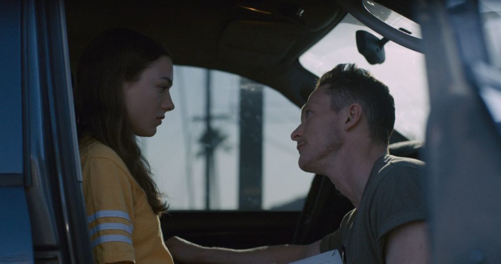 Still from Palm Trees and Power Lines. Lily McInerney stars as Lea and Jonathan Tucker stars as Tom in Jamie Dack's feature debut film Palm Trees and Power Lines. This image accompanies the review of Palm Trees and Power Lines. The pair are in Tom's truck, and he's crouched in front of her; she is sitting in the front seat.