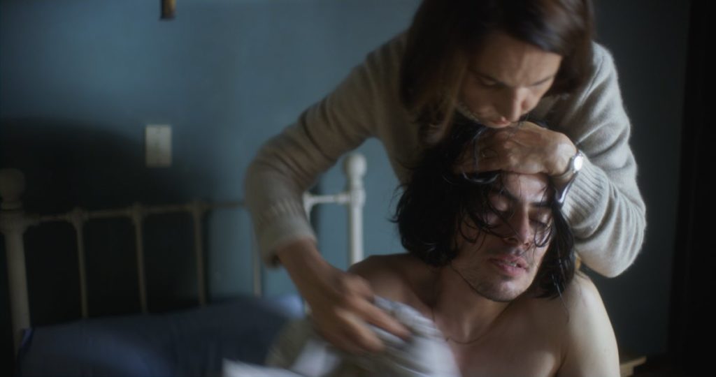 Carmen (Aline Kuppenheim) nurses Elías (Nicolás Sepúlveda) back to health in Manuela Martelli's film Chile 1976. Elías looks sickly while seated on a bed. Carmen stands over him with a wash cloth, her hand on his head.