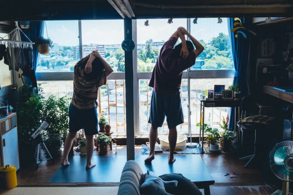 Yo and Teruo do their morning stretches in Teruo's apartment in Daigo Matsui's film Just Remembering. They are looking out the window, their backs facing us, moving in sync.