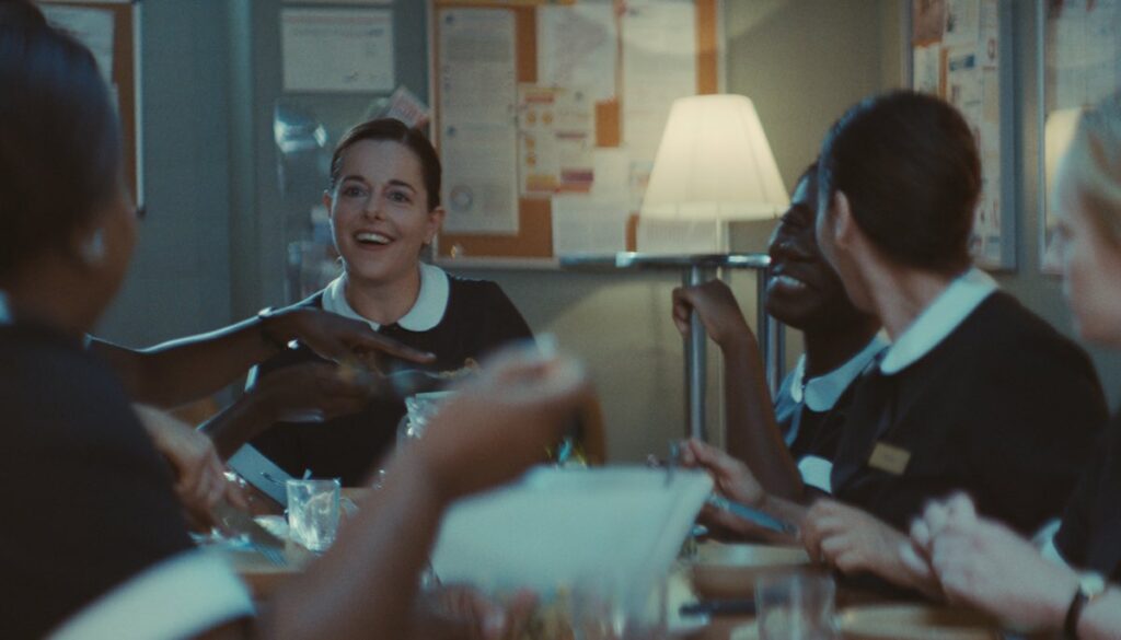 Laure Calamy stars as chambermaid Julie in Éric Gravel's second feature film, Full Time. Julie is at the back of the frame, seated at the head of the lunch table, surrounded by her chambermaid team, all dressed in their black and white uniforms.