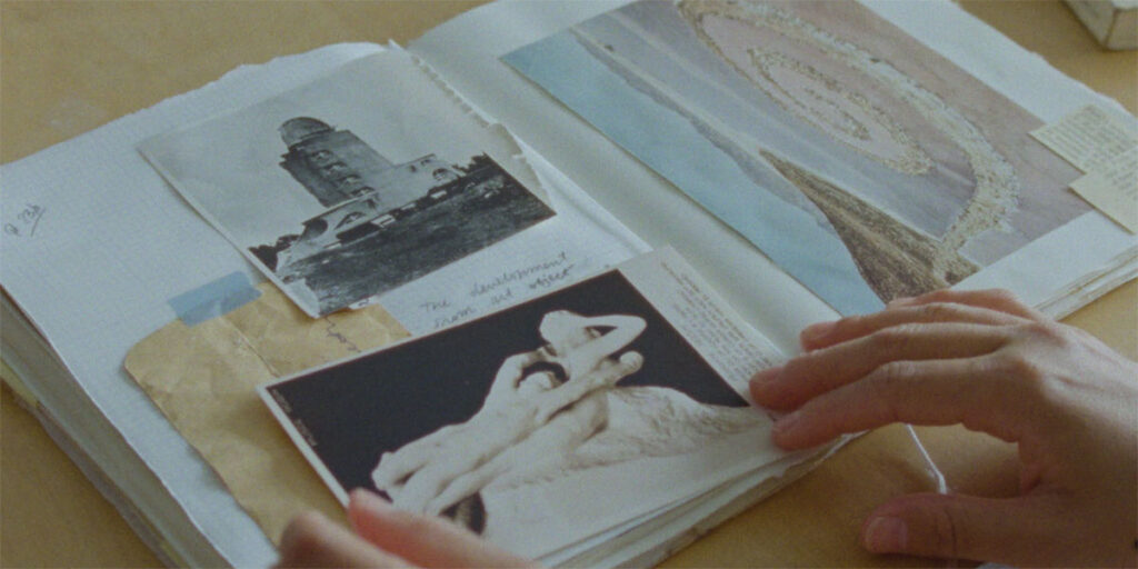 Still from Rita Ferrando's Pleasure Garden, one of the best and must-see shorts at TIFF 2022. A woman's hands are seen touching a scrapbook of photographs and postcards of artwork.