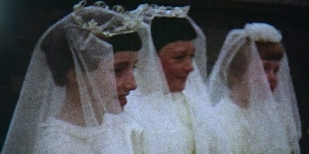 Still of archival footage from Sinéad O'Shea's documentary Pray for Our Sinners, a film which Alex Heeney reviews. Three girls dressed in white with white veils attend their confirmation in this grainy image from archival 16mm film.