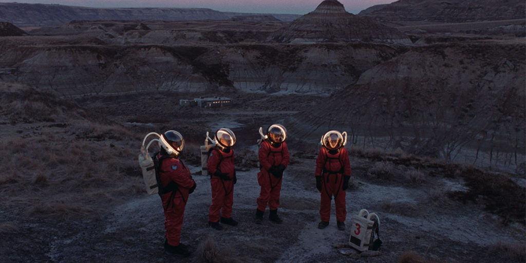Viking was one of the best films of TIFF 2022. Four people dressed like astronauts in red suits stand against a vast desert backdrop in Stéphane Lafleur's Viking. 