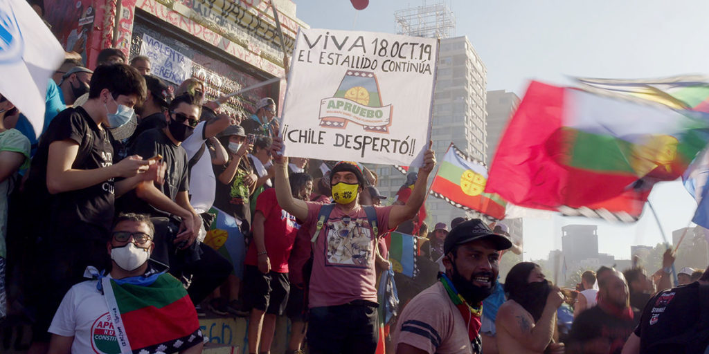 Still from Patricio Guzmán's My Imaginary Country, one of the best films of TIFF 2022. A group of people (mostly in masks) gather in the streets of Santiago with signs and flags in 2021.