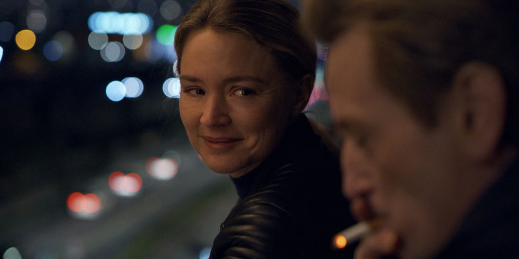 Virginie Efira stars as Mia in Alice Winocour's Paris Memories, one of the best films at TIFF 2022. A blonde woman in a leather jacket looks at a middle-aged man smoking. They are standing on a balcony overlooking the road.
