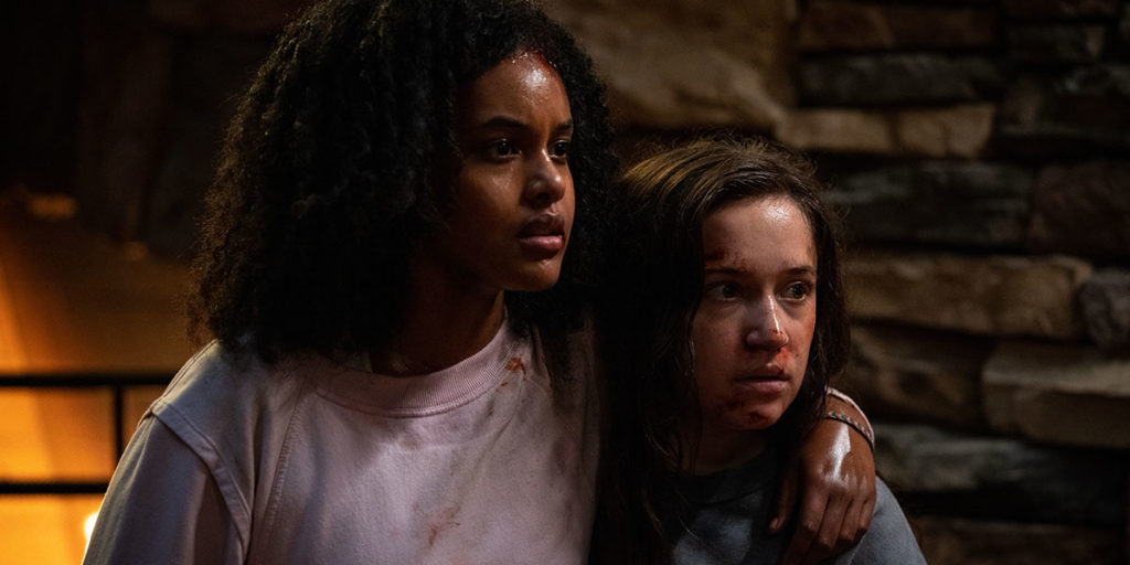 Still from John Hyams's COVID thriller Sick, one of the best films at TIFF 2022. Two young women, one Black and one white, are covered in blood, holding each other, looking ahead in fear.