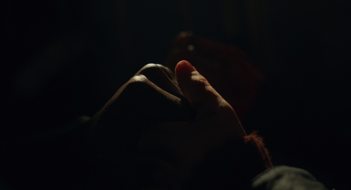 Still of a Black man's hand and a white woman's hand (Mia) in Revoir Paris, directed by Alice Winocour, who we interview about the film in this piece.