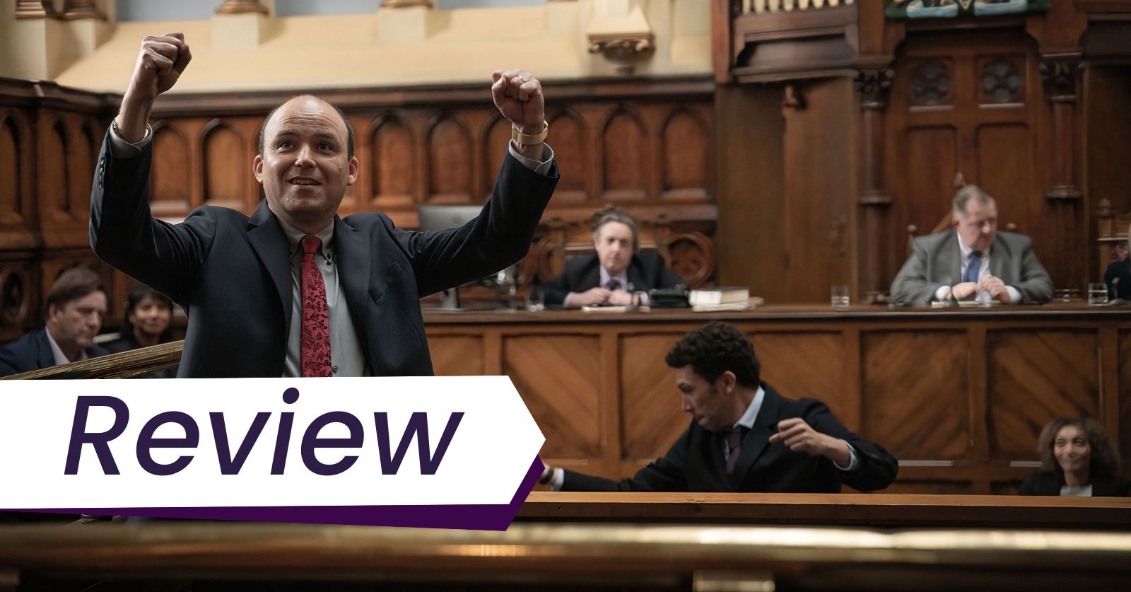 Rory Kinnear (left) and Joely Fry (right) star in the new film Bank of Dave. Photo courtesy of Samuel Goldwyn films. Dave is standing with his fists in the air in a courtroom after winning his case. Hugh is seated behind him also with his fists in the air. Two magistrates can be seen sitting behind them.