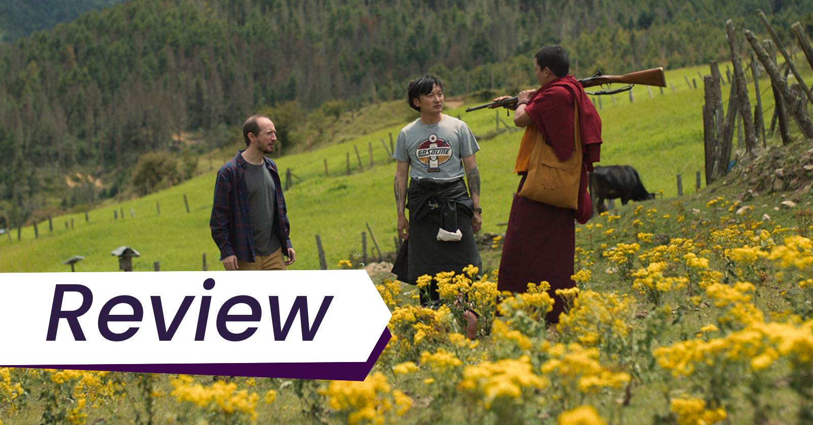 An American, his Bhutanese guide, and a monk holding a gun discuss the gun in The Monk and the Gun, directed by Pawo Choyning Dorji. They are standing on a large field with yellow flowers in the foreground and a hilly forest in the background.