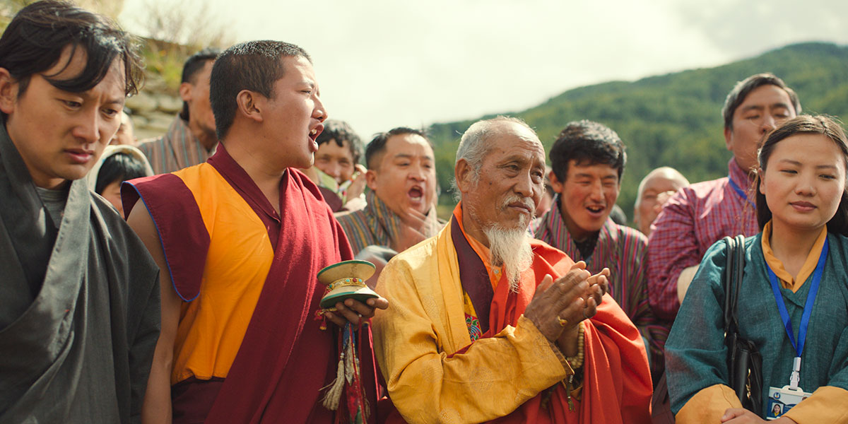 The Monk and the Gun is one of the best acquisition titles at TIFF 2023. Two monks are surrounded by people at an event held in The Monk and the Gun.