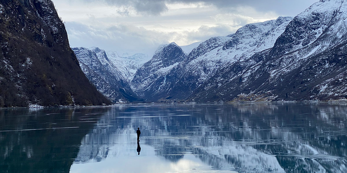 Still of a man walking on a frozen lake against a mountainous backdrop in Songs of Earth. Courtesy of TIFF