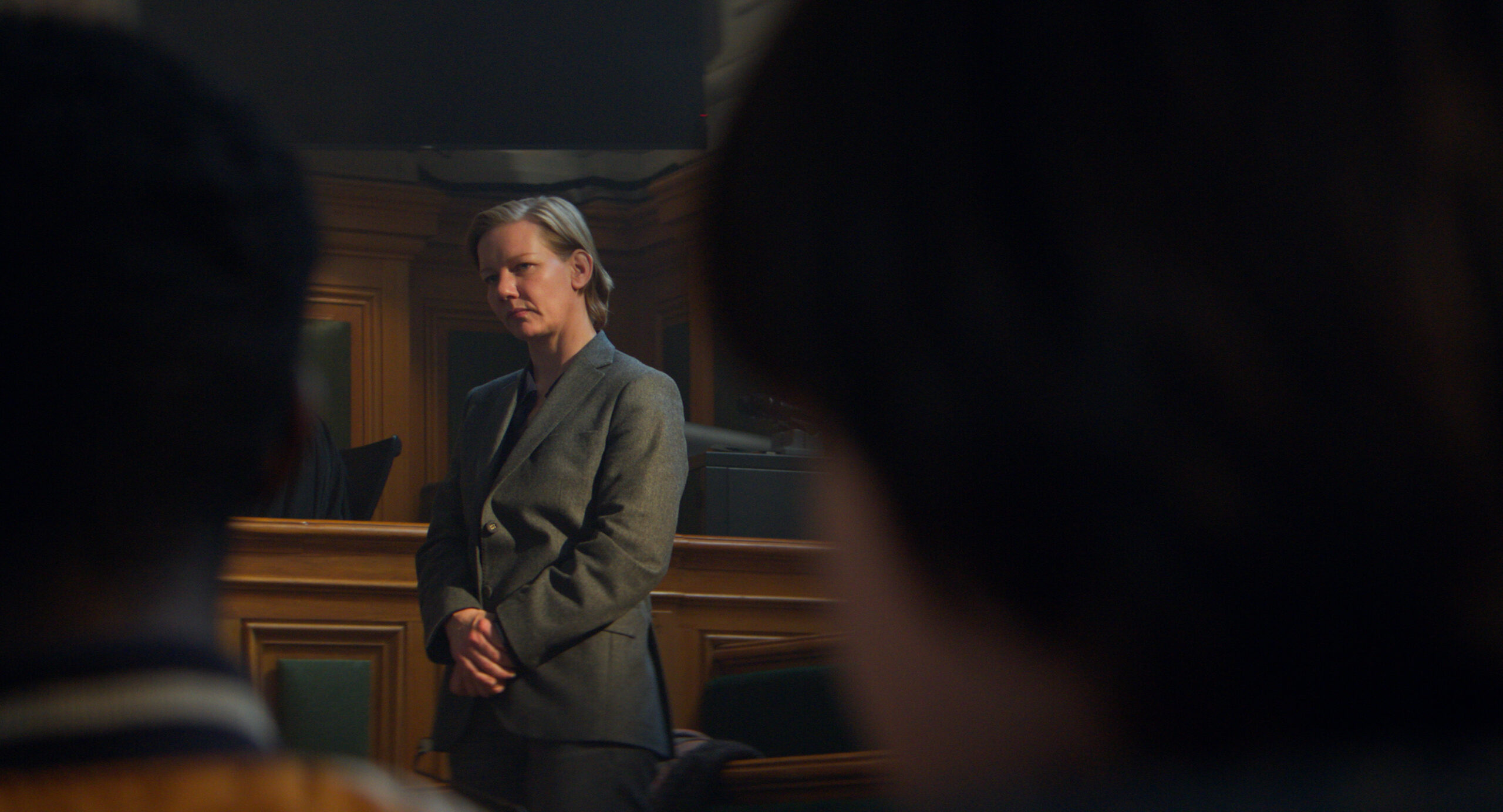A woman in a grey pants suit stands in a court of law and is flanked by two heads in the audience in Justine Triet's Anatomy of a Fall. The festival also includes Fancy Dance, National Anthem, The Promised Land, and more.