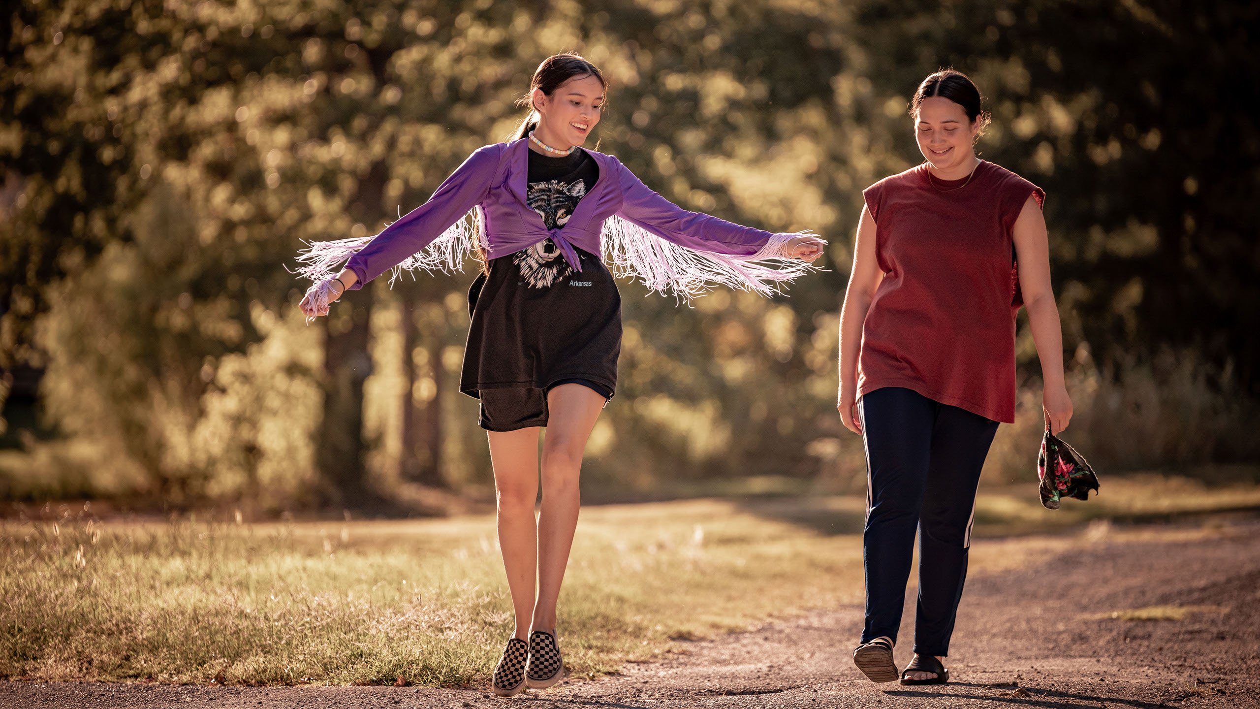 An Indigenous girl in a purple sweater spreads her arms while walking down a green lane with a thirtysomething woman played by Lily Gladstone in Fancy Dance. The festival also includes Fancy Dance, National Anthem, The Promised Land, and more.