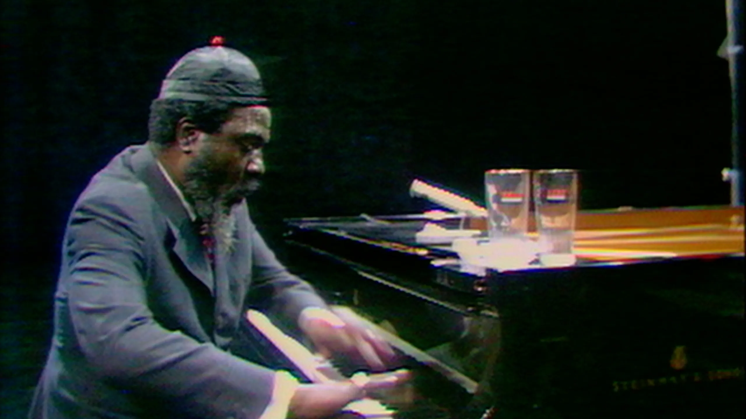 Still of Thelonius Monk, a Black man in a suit and a black cap playing a grand piano, in Rewind & Play, one of the best films of 2023