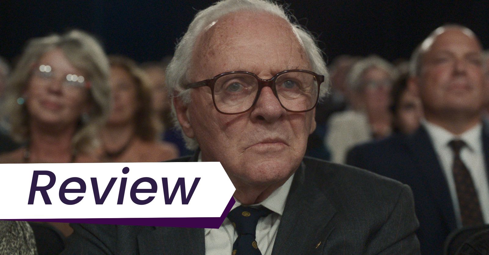 Still of Anthony Hopkins as Nicholas Winton in James Hawes's One Life. Photo courtesy of Bleeker Street Films. An elderly white man with white hair and glasses wearing a suit sits at the front of an audience in James Hawes's One Life.