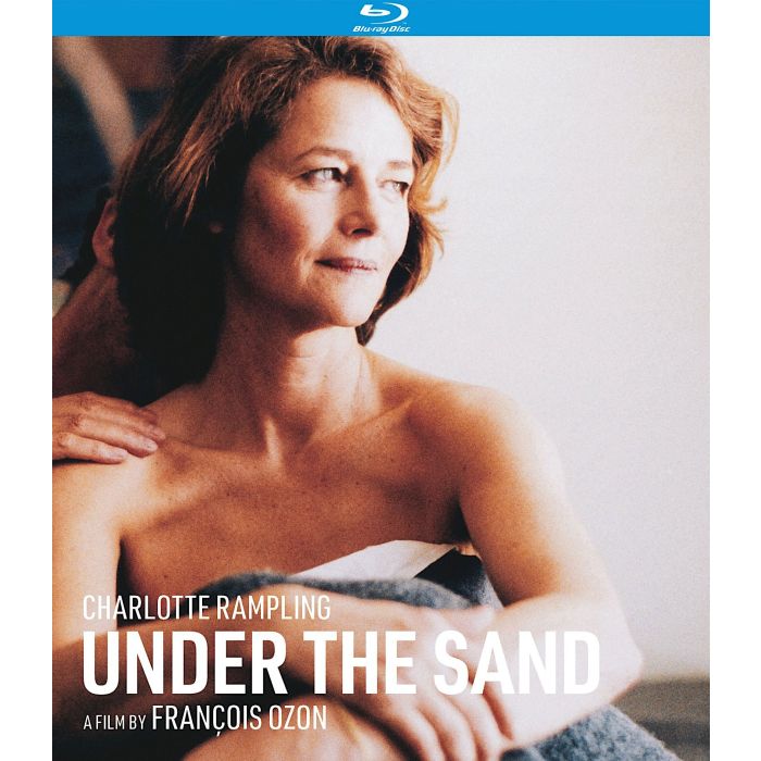 Cover of the Blu ray of François Ozon's Under the Sand, one of the best 5 films to buy in the 2024 Kino Lorber Summer Sale. Charlotte Rampling is seen in bed, shoulder bare, underneath a blanket, while a man caresses her from behind.