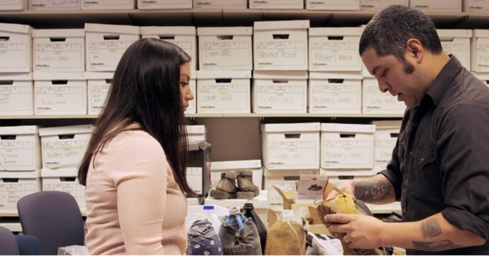 A man and a woman stand in an office surrounded by file boxes